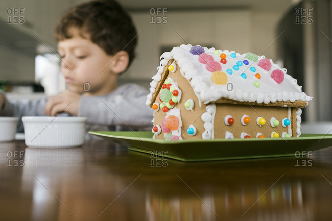 Boy sitting at a table with a decorated gingerbread house