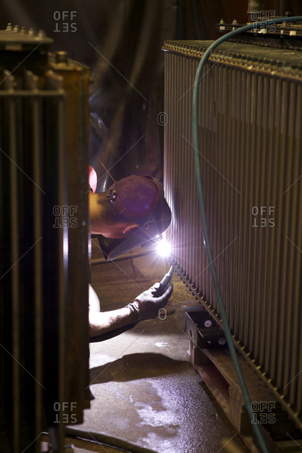 Welder working on a component of an electrical transformer in factory