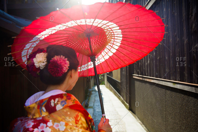 Woman in traditional clothing with an oil paper umbrella in an alleyway in Kyoto, Japan