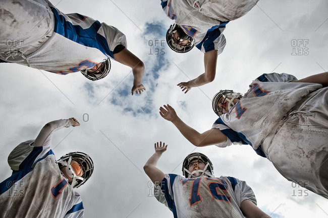 A group of American football players in sports uniform and protective helmets, in a team huddle viewed from below