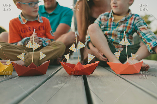 Family of four sitting on a dock looking at paper boats
