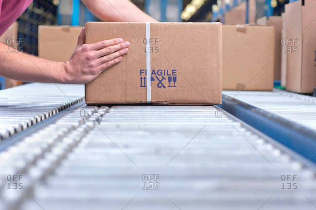 Hands of worker packing box on conveyor belt in distribution warehouse