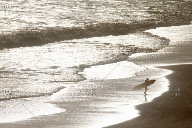 Surfer carrying surf board, walking along beach from sea