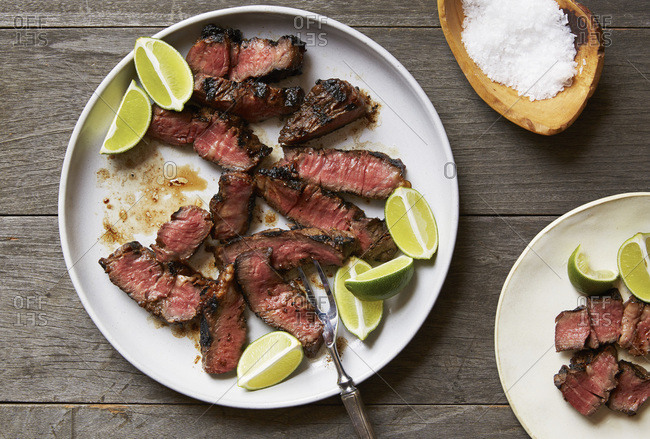 Sliced grilled steak with lime wedges