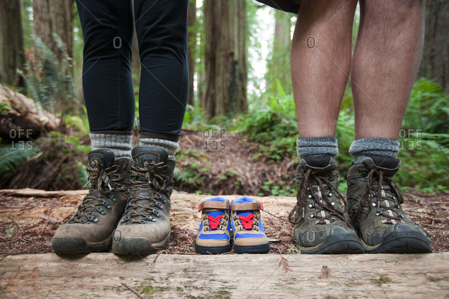 Expecting parents use a pair of small hiking boots in line with their own to announce the arrival of their new baby