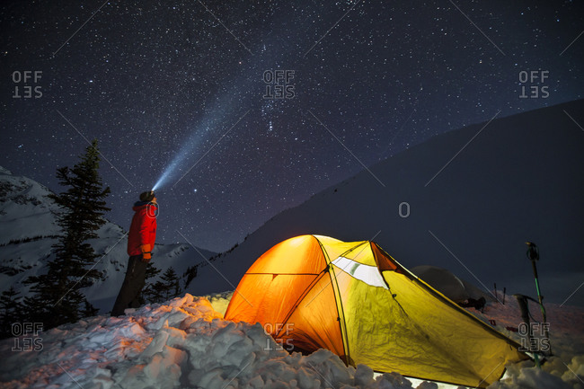 Climber standing beside his lit up tent under a starry night sky near Whistler, British Columbia, Canada