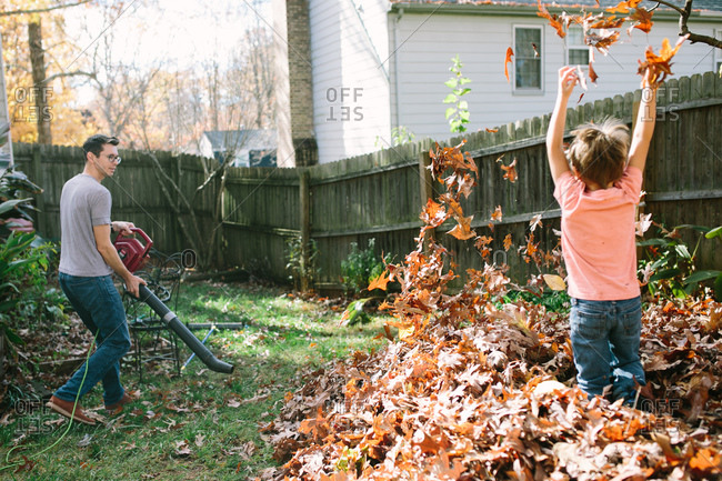 Boy playing in leaves as his dad uses a leaf blower