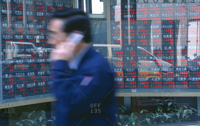 Blurred motion of a man walking in front of a stock market display board in Tokyo, Japan