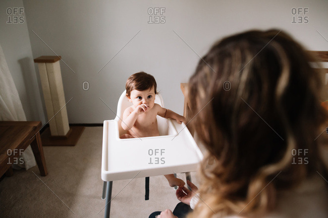 Baby boy sitting in a high chair while his mother tickles his feet