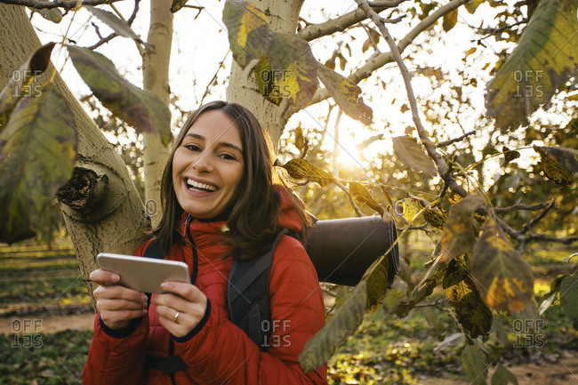 Portrait of happy female hiker with cell phone at a tree