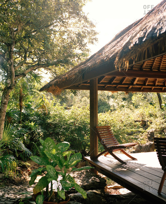 Thatched roof outdoor pavilion with chairs in tropical landscape