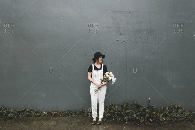 Woman in white overalls with a bouquet of white flowers against a black wall