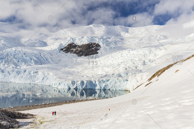Two hikers surrounded by ice-capped mountains and glaciers in Neko Harbor, Antarctica