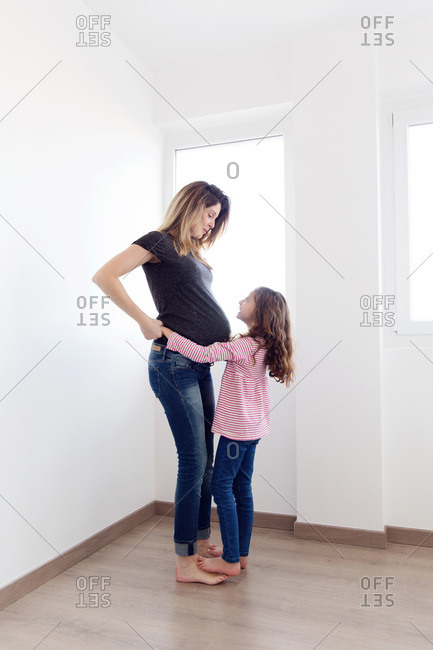 Daughter hugging her pregnant mother in corner of white room