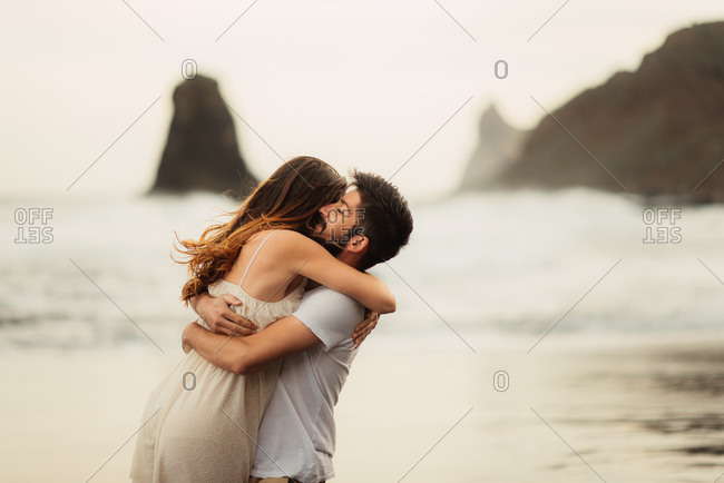 Man lifts his partner while embracing her on beach