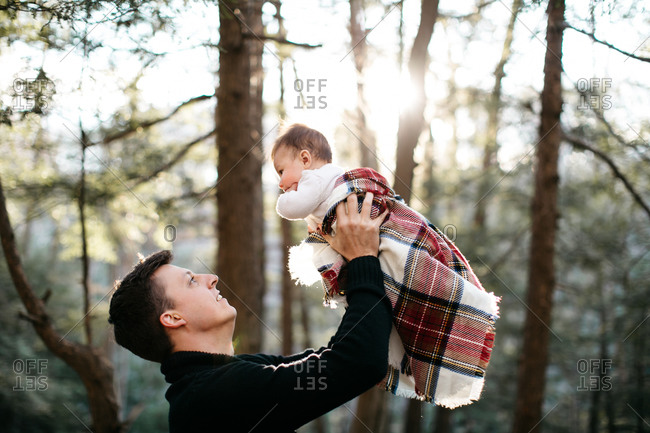 Father lifting baby boy wrapped in blanket in woods