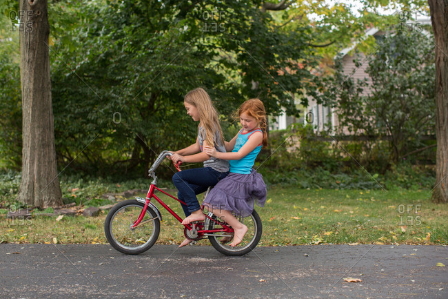 Two girls peddling on a red banana seat bicycle
