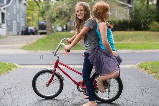 Two girls sitting back to back banana seat bicycle