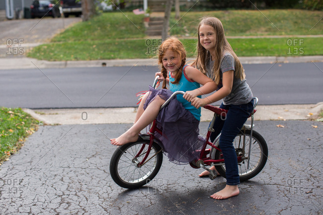 Two girls on a banana seat bicycle with one riding on the handlebars