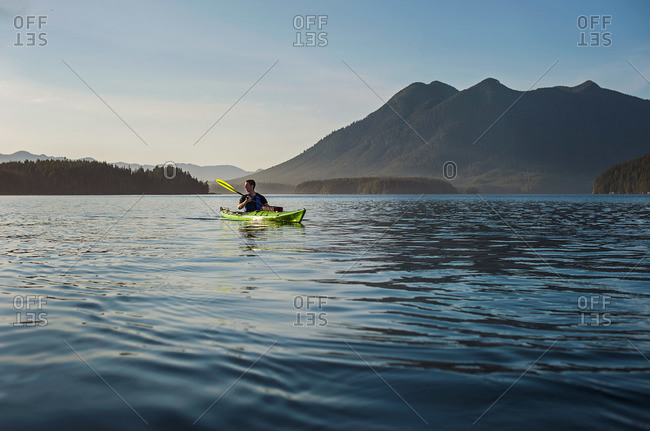 Man in kayak paddles in beautiful calm mountain lake