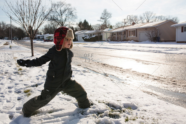 Boy in snow gear throws a snowball into the street