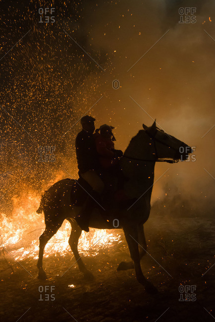 A man and a little girl ride a horse next to a bonfire during \'Las Luminarias\' Festival. In honor of Saint Antony, the patron saint of animals, horses are ridden through the bonfires to purify and protect the animal during the year ahead