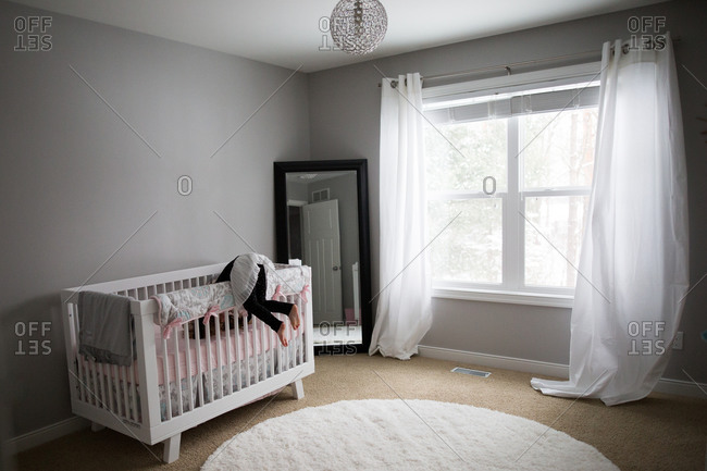 Girl climbing over the crib rail in her sibling\'s nursery