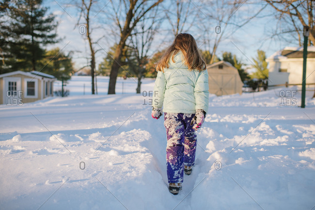 Girl with snow-covered pants walking through a path in the snow