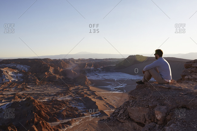 Man sitting on a cliff watching the sun set over a desert valley