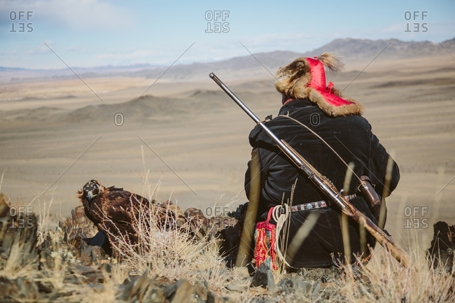 Mongolian hunter and his golden eagle wait on hillside during a hunt