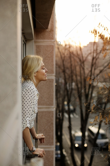 Woman in polka dot blouse standing on a balcony with eyes closed