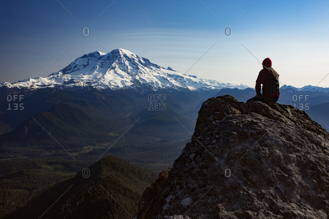 Man sitting on top of a mountain peak taking in the view