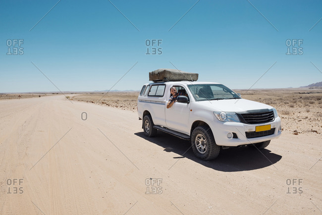Man on a 4x4 car with tent on the roof in a dusty road in Namib desert