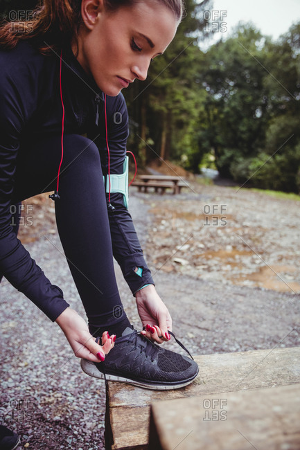Close up of fit brunette with armband tying her shoe lace in the woods