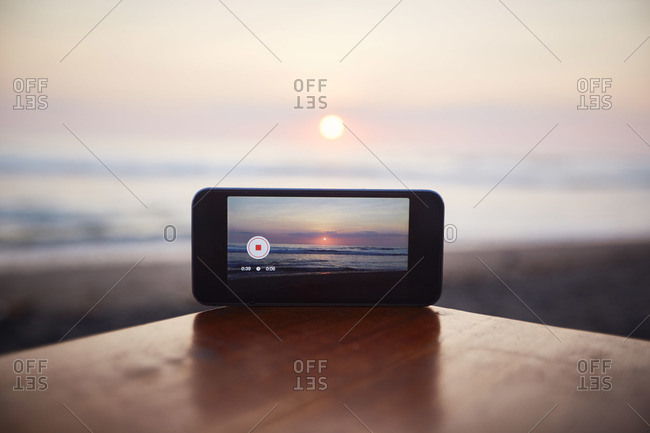 Smartphone sitting on a beachside table taking a video of a sunset