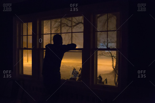 Person silhouetted at window watching snow