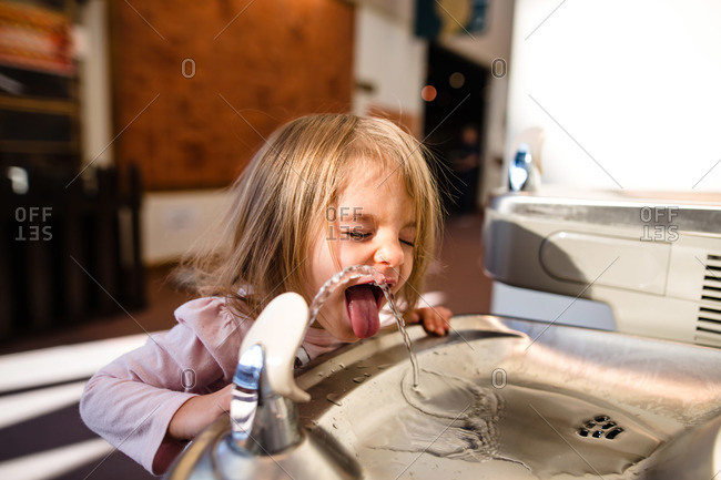 Toddler girl closes her eyes while getting a drink from water fountain