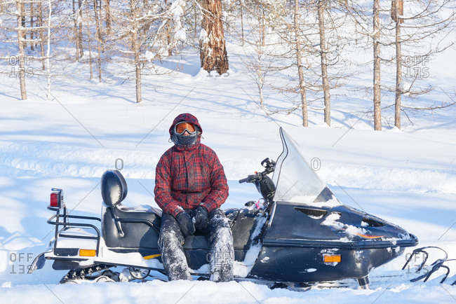 Young man with snow-covered pants sitting on a snowmobile