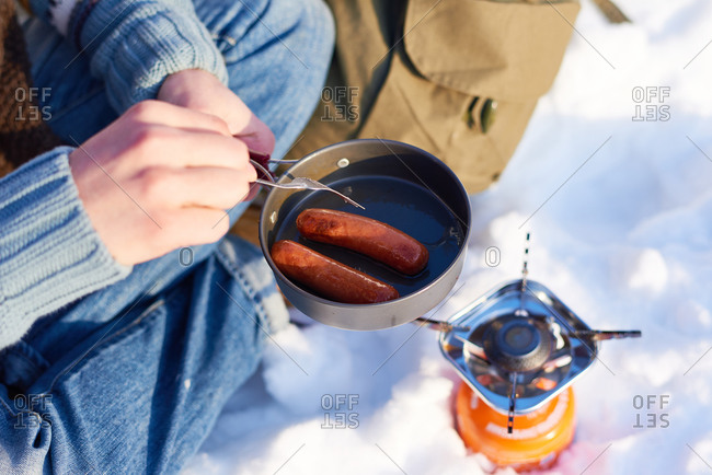 Man cooking sausages over a campstove in the snow