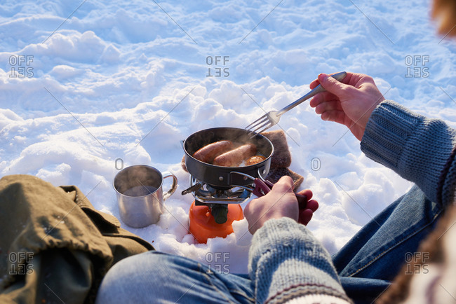Man stirring sausages in a pot in the snow