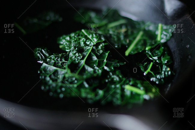 Leaves of green kale cooking in a cast iron skillet
