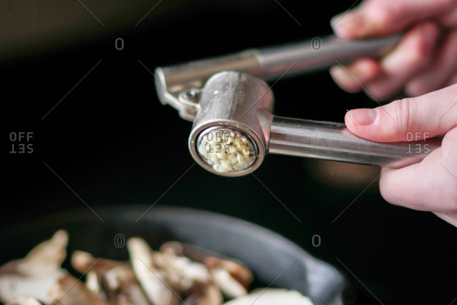 Hands using a garlic press to crush garlic
