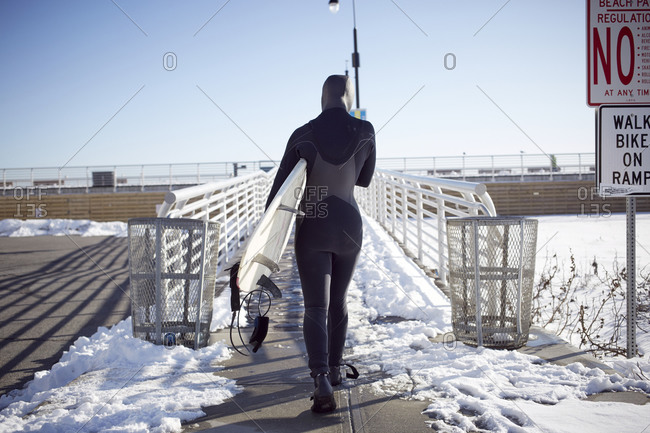 Teenage girl in wetsuit carrying surfboard in winter