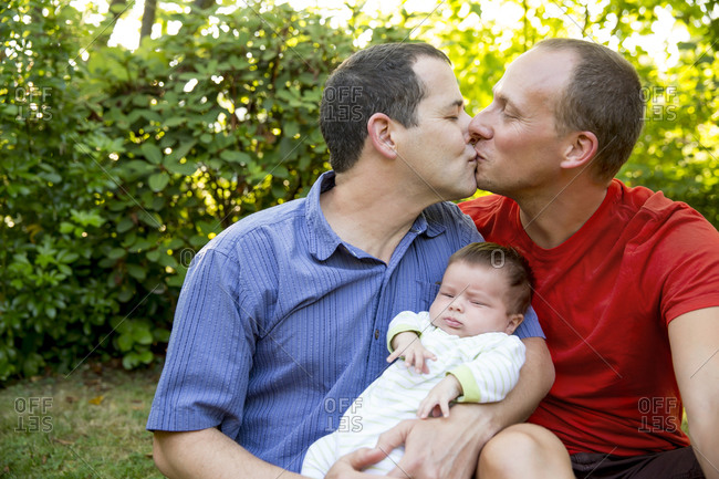 Gay couple kissing with baby boy in backyard