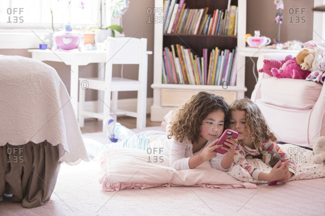Girls using cell phone on bedroom floor
