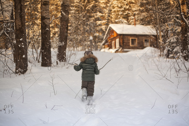 Boy walking in snowy field towards log cabin