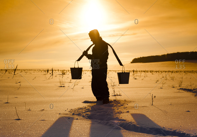 Silhouette of Man carrying buckets on traditional yoke in snowy field