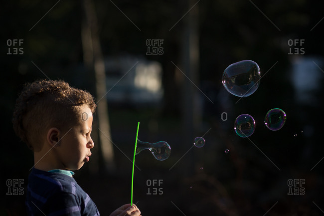Boy watches bubbles form while blowing into a bubble wand