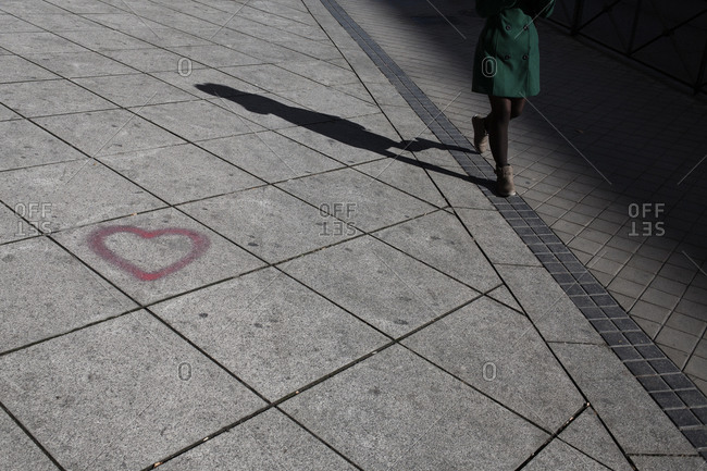 Woman walking down the sidewalk past a graffiti heart