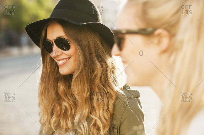 Happy woman in sunglasses at hat with friend on street